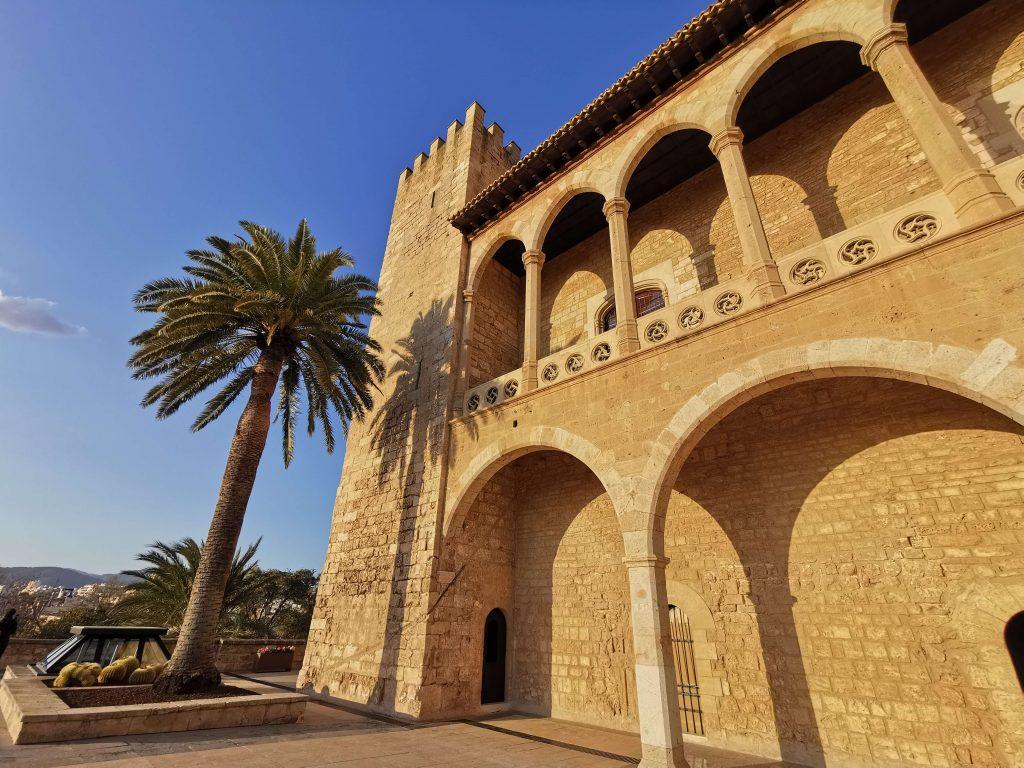 Gotische Fassade des Palacio Real de la Almudaina mit Palmen im goldenen Licht