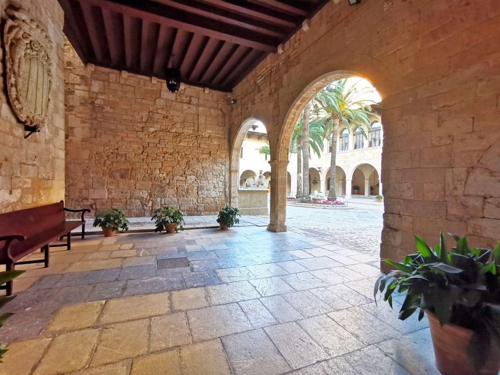Blick aus dem schattigen Innenhof mit Bank auf Arkaden und Palmen im Palacio Real de la Almudaina