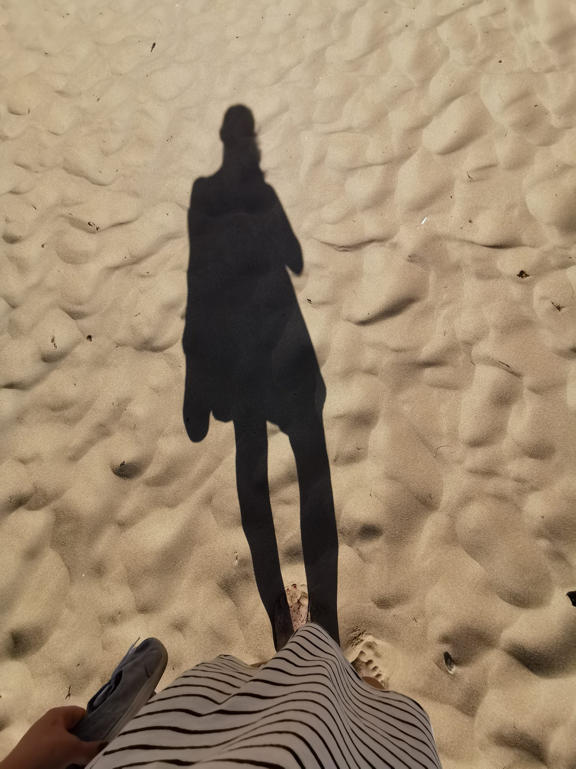 Schatten einer Frau auf einem Sandstrand.