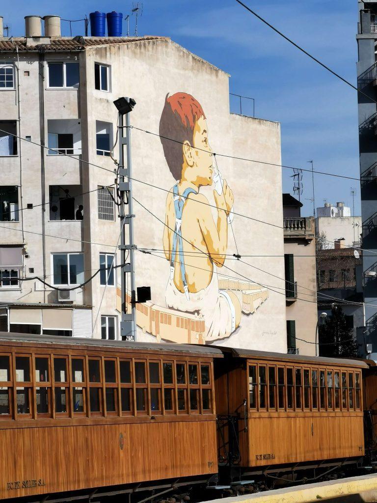 Historischer Holzzug des Tren de Sóller vor Wandbild mit Kind und Zug