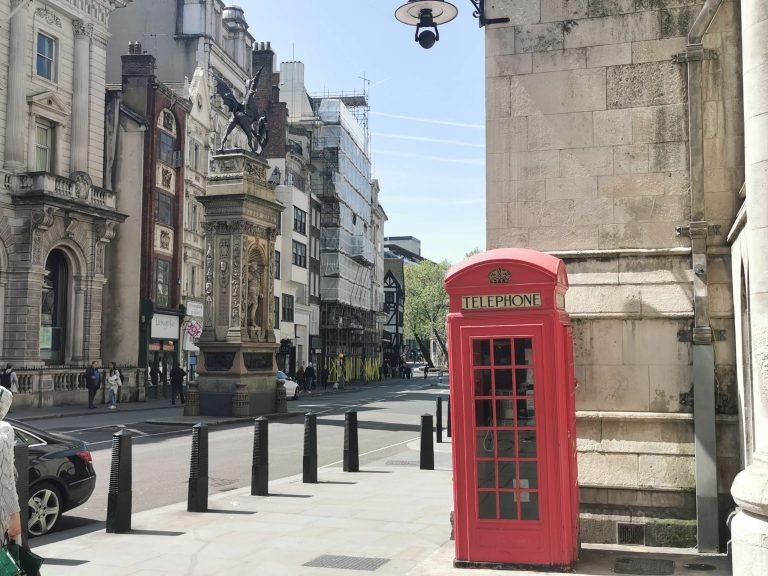 Rote Telefonzelle an einer Straßenecke in London bei Tageslicht – typisches Stadtbild, ruhig und klar