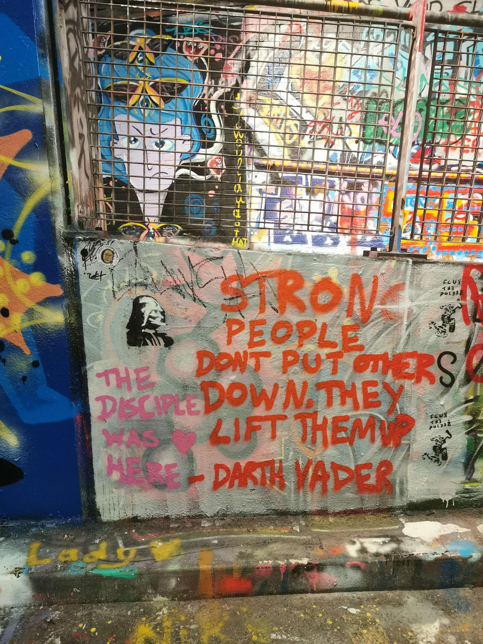 Streetart im Leake Street Tunnel London mit dem Spruch ‚Strong people don’t put others down, they lift them up – Darth Vader‘ in roter Schrift auf grauer Wand