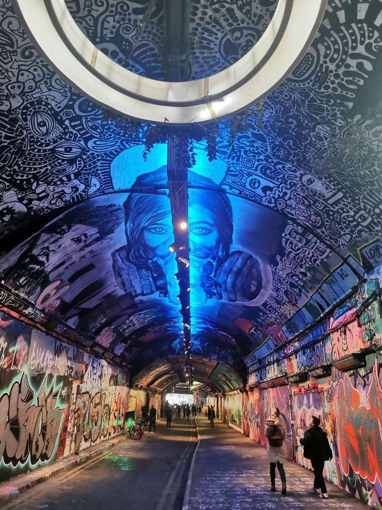 Streetart im Leake Street Tunnel in London mit großem Wandbild eines Gesichts und blauer Beleuchtung.