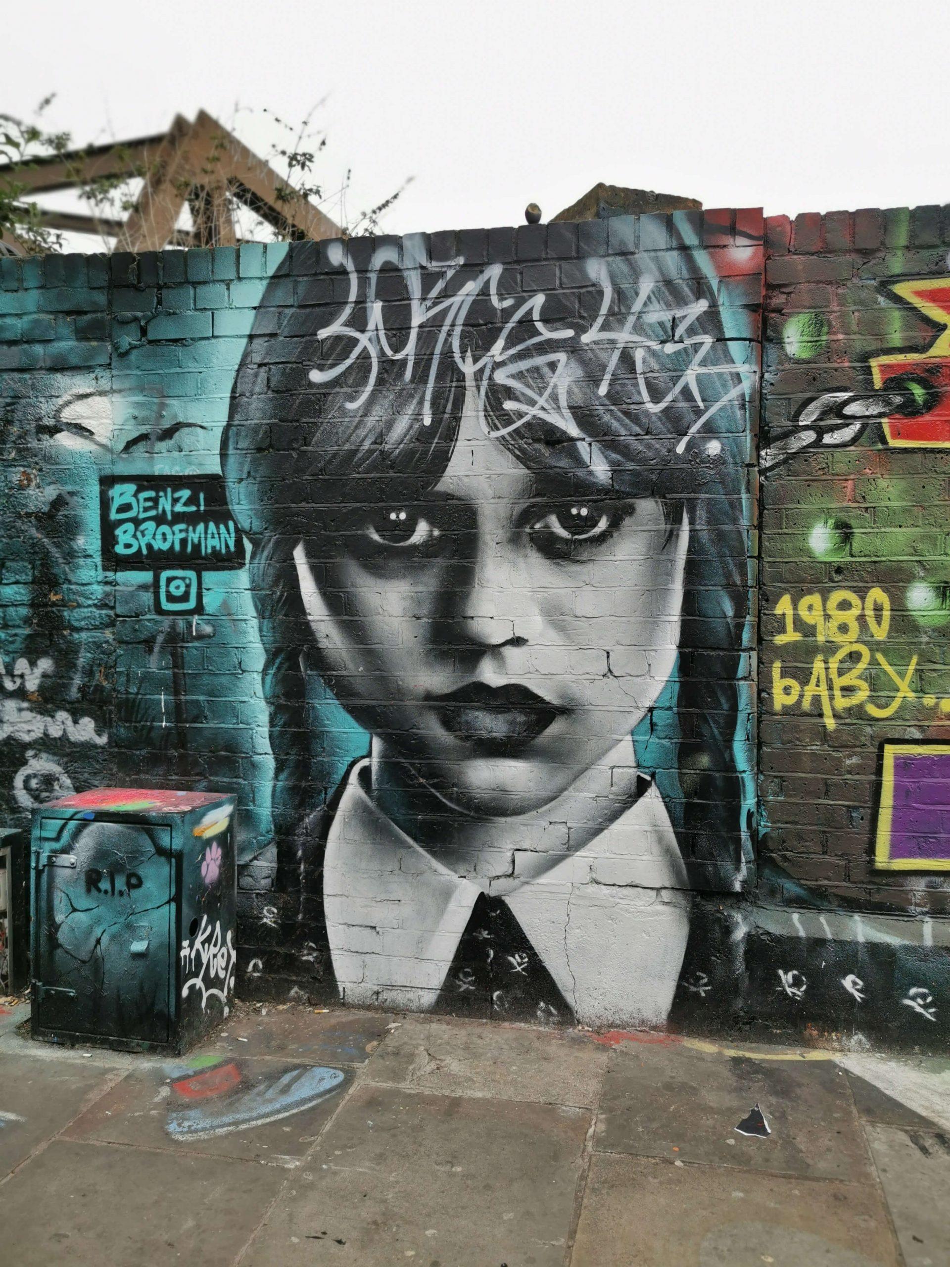 Streetart in London: Schwarz-weißes Porträt von Wednesday Addams mit türkisfarbenem Hintergrund, gesprüht auf eine Wand