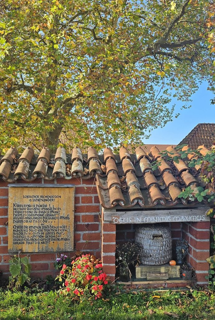 Gedenkstelle am Domhof in Ratzeburg mit dem Lorscher Bienensegen, einer alten Inschrift auf Holz neben einem traditionellen Bienenkorb unter Ziegeldach.