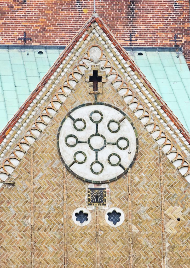 Detailansicht der Fassade des Ratzeburger Doms mit Backsteinornamenten und runder Fensterrose unterhalb des Giebels.