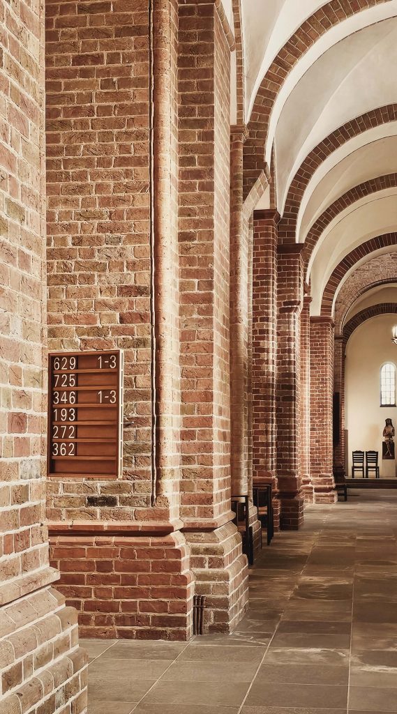 Innenaufnahme des Ratzeburger Doms mit rötlichen Backsteinbögen, hellen Gewölbedecken und warmem Licht.