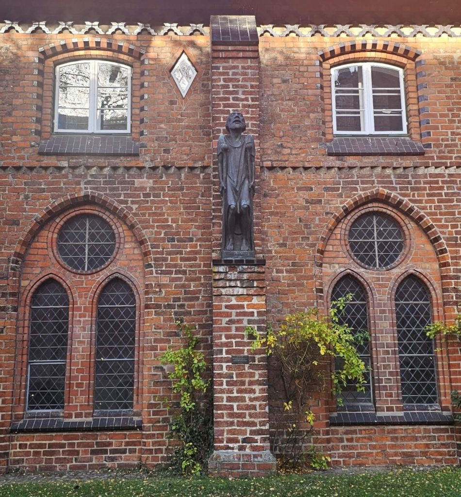 Backsteinfassade am Ratzeburger Dom mit gotischen Fenstern und einer bronzenen Skulptur von Ernst Barlach an der Mauer.