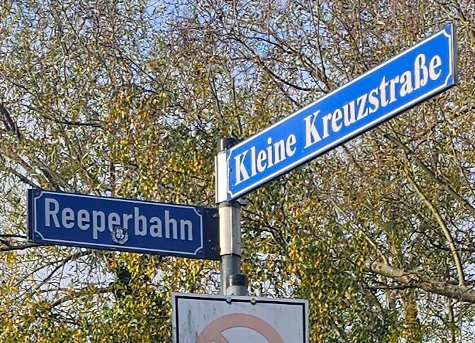 Blaue Straßenschilder „Reeperbahn“ und „Kleine Kreuzstraße“ in Ratzeburg, an einer Kreuzung mit herbstlichen Bäumen im Hintergrund.