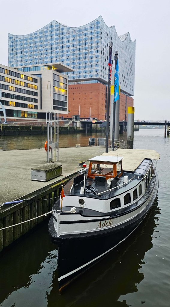 Das Boot „Adele“ auf einem Kanal in Hamburg mit Blick auf die Elbphilharmonie – typische Herbstszene zwischen Speicherstadt und HafenCity.