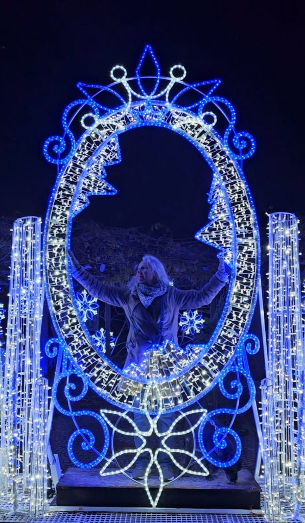 Person steht in einem blau-weißen leuchtenden Märchenspiegel im Christmas Garden Mainau