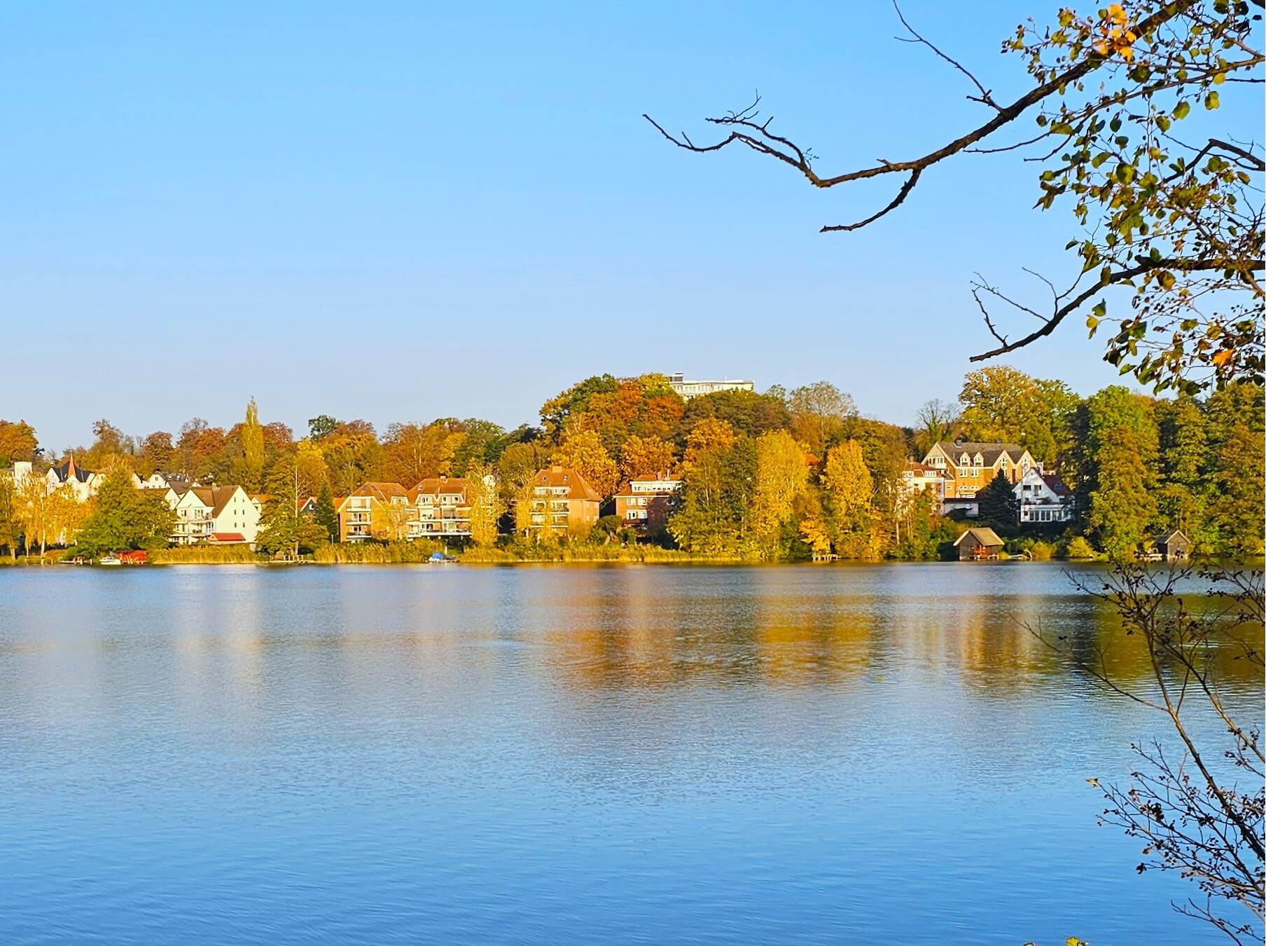 Blick über den Ratzeburger See auf die herbstlich gefärbten Uferhäuser in der Sonne