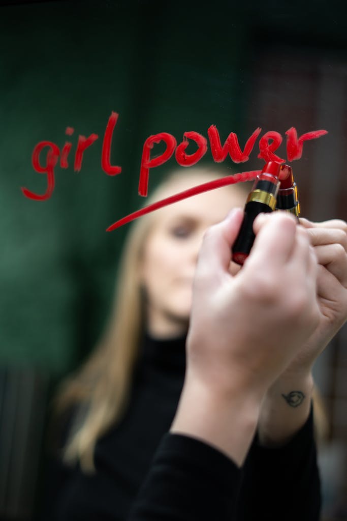 Close-up of 'girl power' written with lipstick on mirror symbolizing empowerment and feminism.
