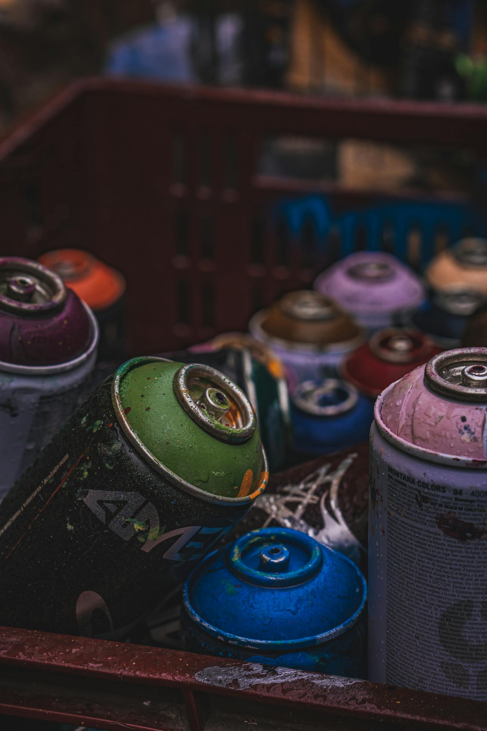 Close-up of vibrant spray paint cans stacked in a crate, highlighting artistic urban tools.