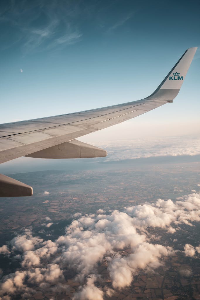 Scenic view of airplane wing flying over clouds and landscape with clear sky.