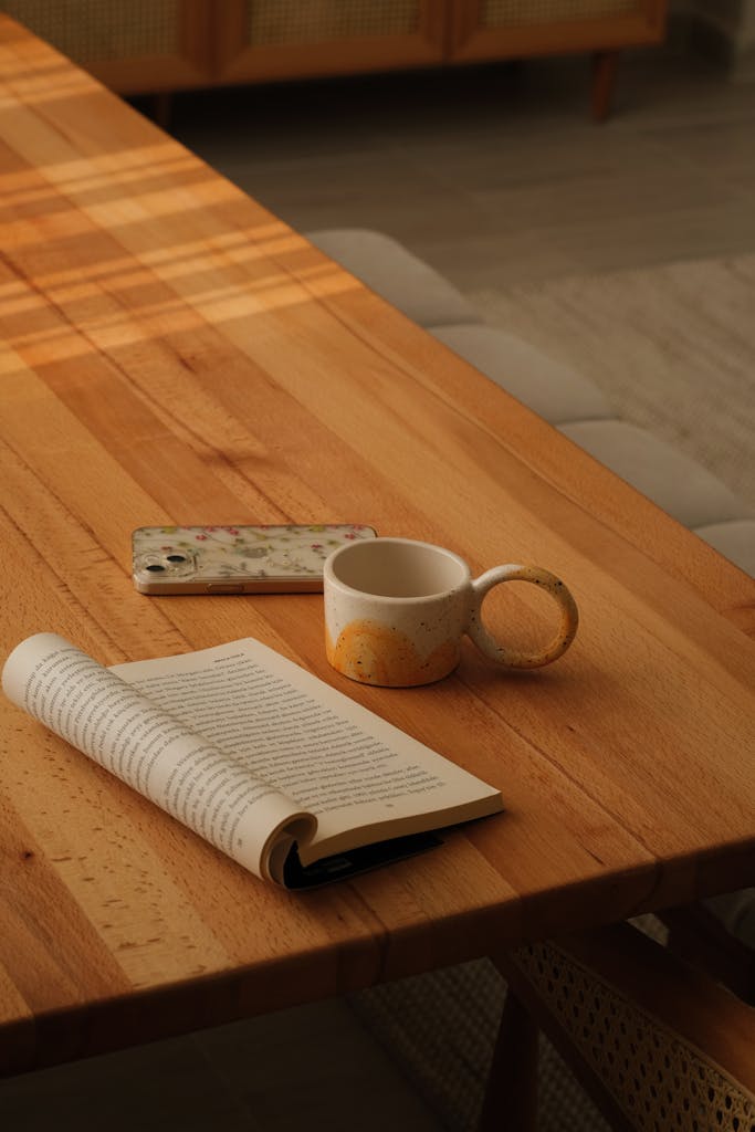 Warm and inviting setting with a book, mug, and phone on a wooden table, perfect for relaxation.