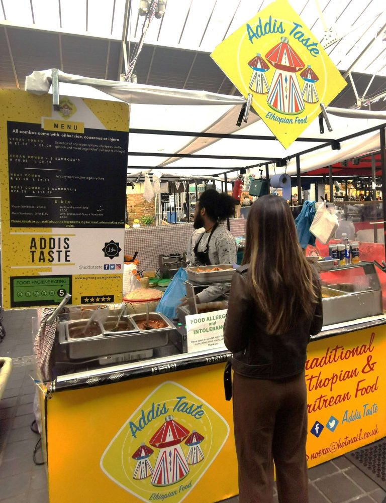 Frau vor einem Streetfood-Stand mit äthiopischem Essen auf dem Greenwich Market in London