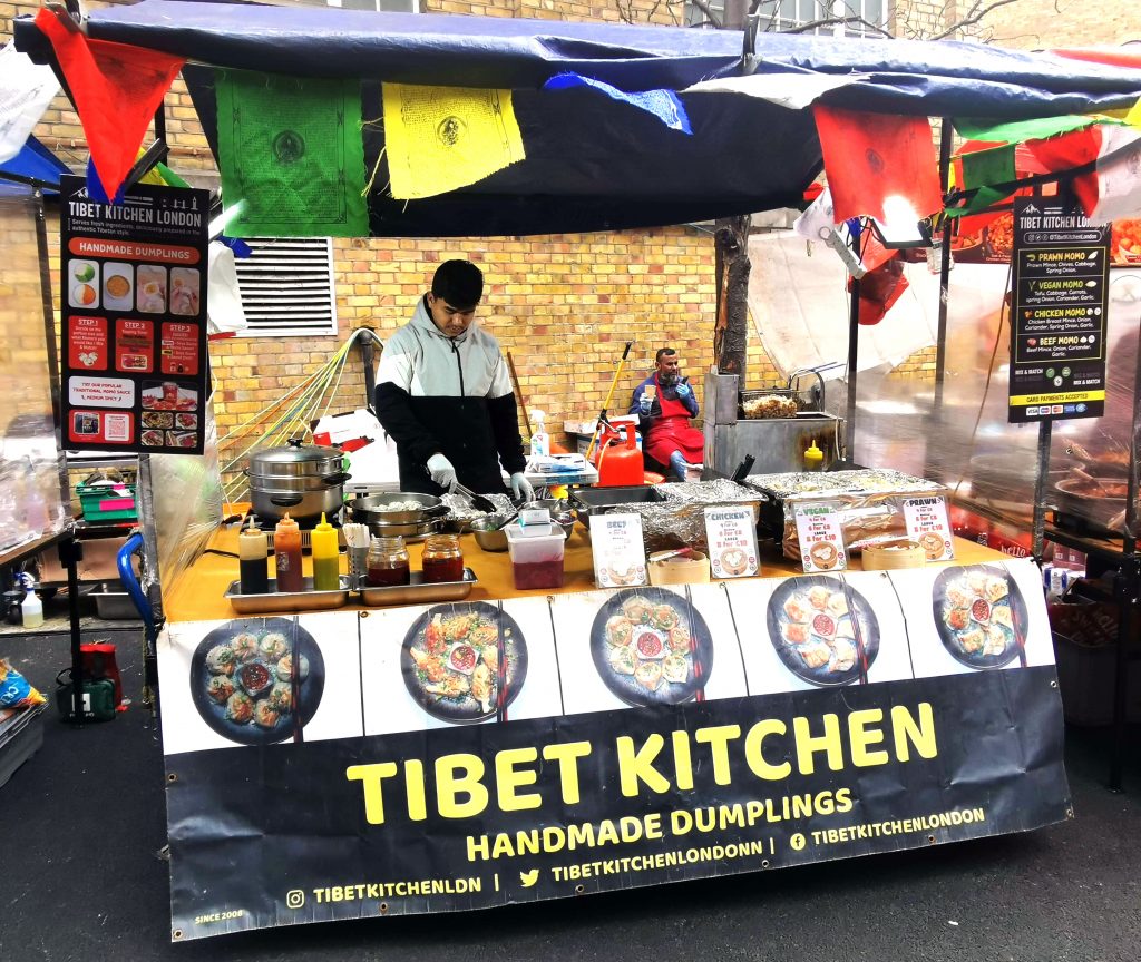 Streetfood-Stand auf dem Brick Lane Market in London mit verschiedenen Gerichten und Marktatmosphäre