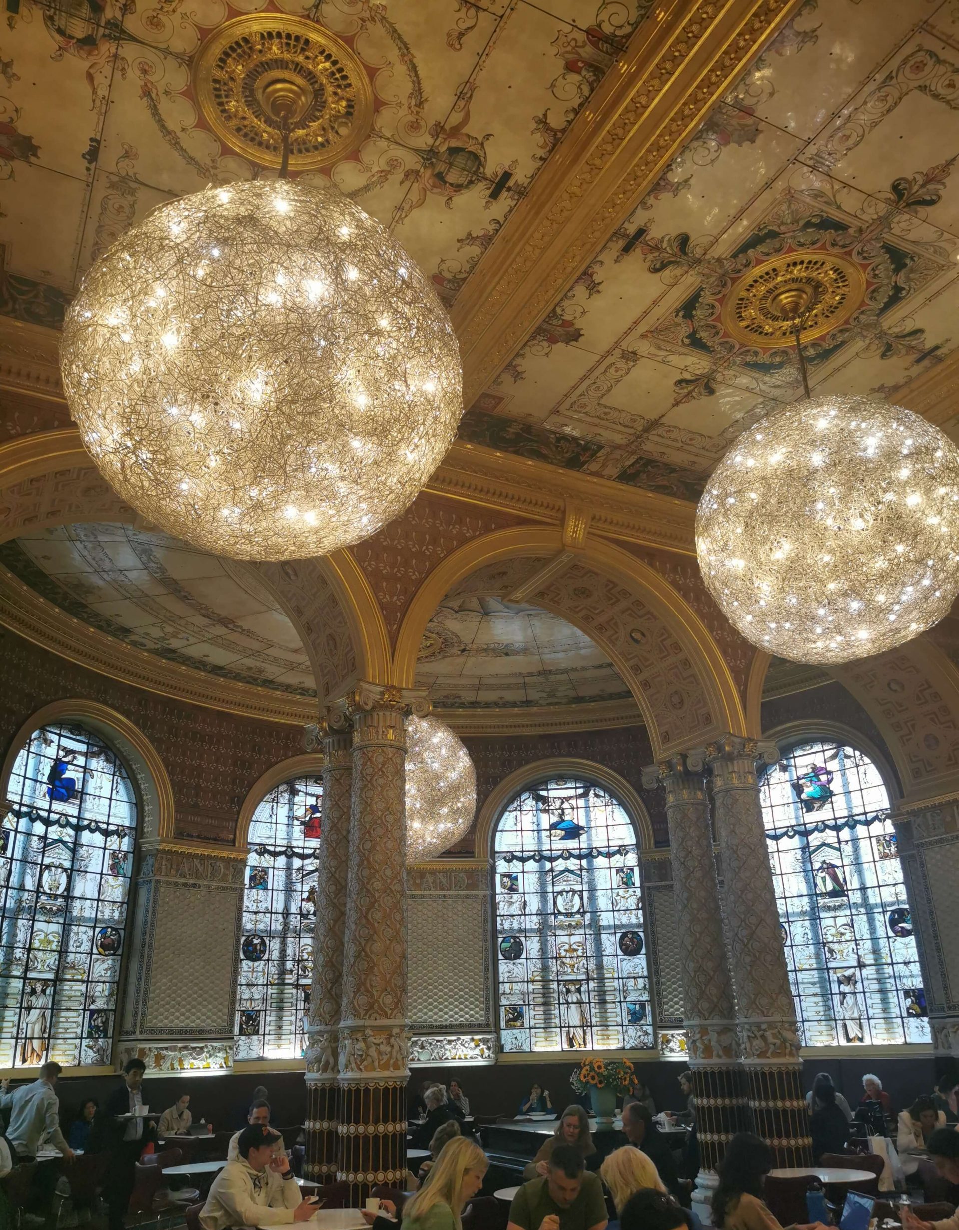 Innenraum des Cafés im Victoria and Albert Museum London mit großen leuchtenden Lampen und verzierten Wänden
