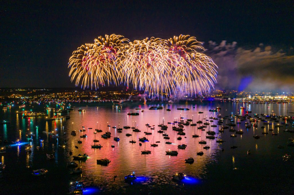 Großes buntes Feuerwerk am Nachthimmel und vielen leuchtenden Booten auf dem Wasser.