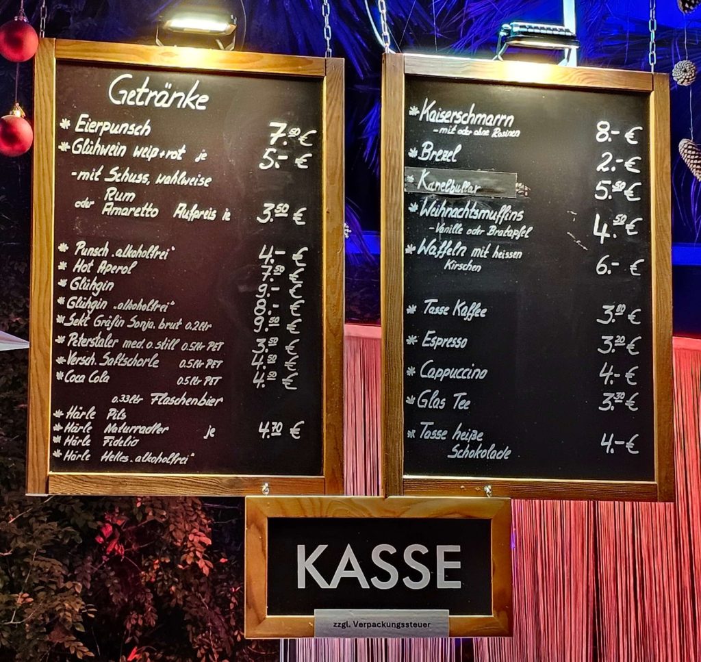 Preistafeln mit Glühwein, Kaiserschmarrn, Waffeln und weiteren Getränken beim Christmas Garden Mainau in der Saison 2025/2026